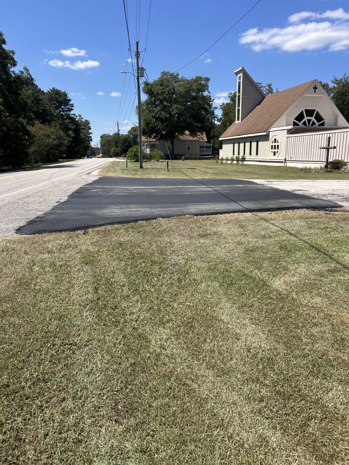 Fresh asphalt entrance and road tie-in beside a church