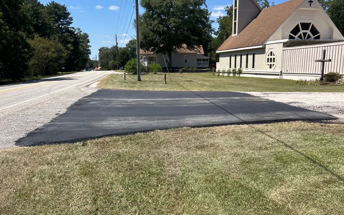 New asphalt entrance patch tied into the road in front of a church